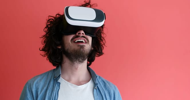 Happy man getting experience using VR headset glasses of virtual reality, isolated on red background