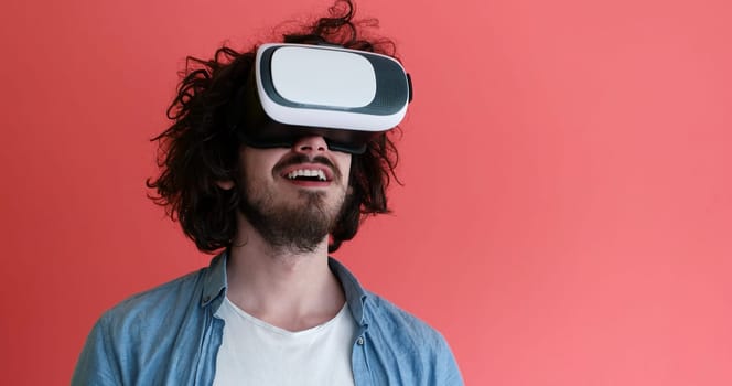 Happy man getting experience using VR headset glasses of virtual reality, isolated on red background