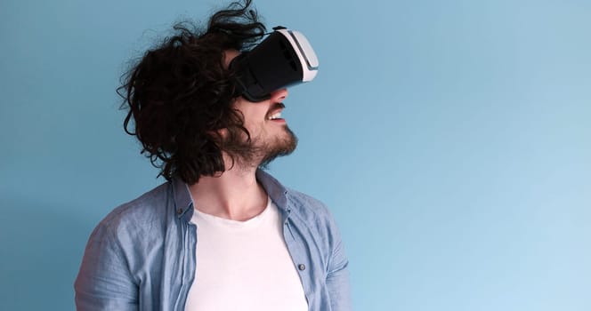 Happy man getting experience using VR headset glasses of virtual reality, isolated on blue background