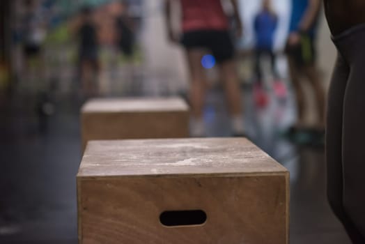 Fit young african american woman box jumping at a crossfit style gym. Female athlete is performing box jumps at gym with focus on legs