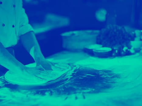 chef preparing dough for pizza rolling with hands on sprinkled with flour table