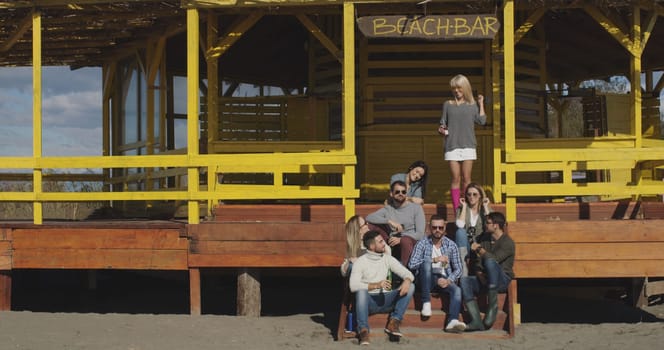 Happy Group Of Friends Hanging Out At Beach House having fun and drinking beer on autumn day