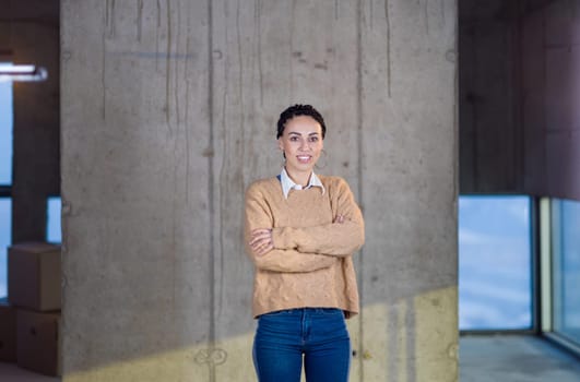 portrait of young successful smiling casual businesswoman standing in front of a concrete wall at new startup office