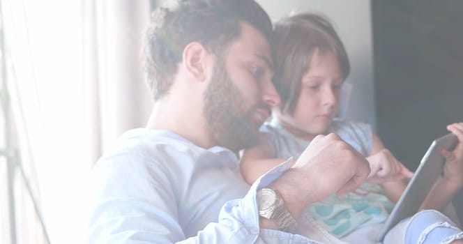 Father Daughter sitting in sofa  playing games on tablet