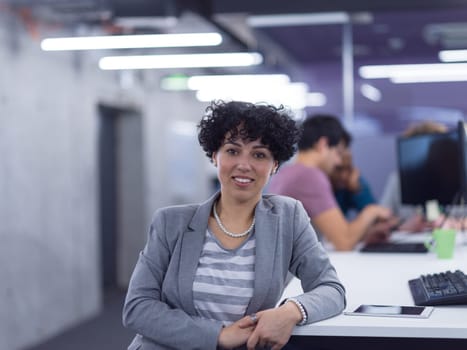 portrait of young female software developer at busy startup office with her multiethnic business team in background