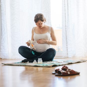 Happy Caucasian pregnant mother is sitting on the floor, touching her tummy, blue jeans