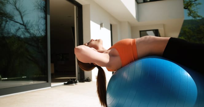 Young Woman Doing Yoga and streching on ball in front of villa