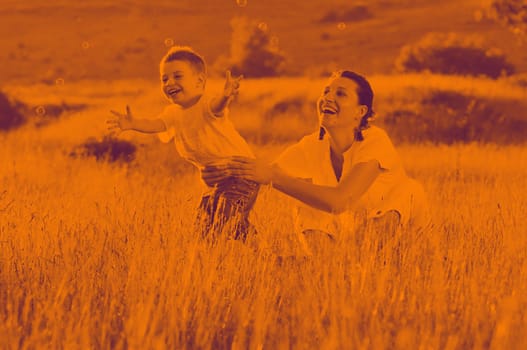 happy child and woman outdoor playing with soap bubble on meadow duo tone