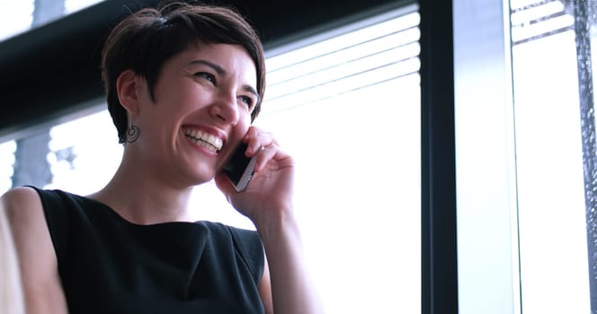 businesswoman speeking on phone beside window of modern office