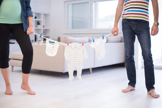 Beautiful pregnant woman and her husband expecting baby holding baby bodysuits and smiling at home
