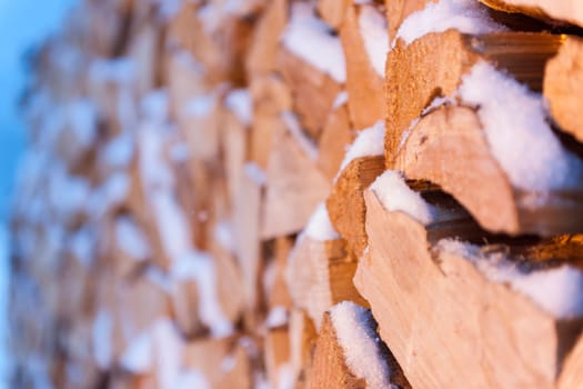 Full-frame side view of freshly chipped, stacked and snow-covered firewood.