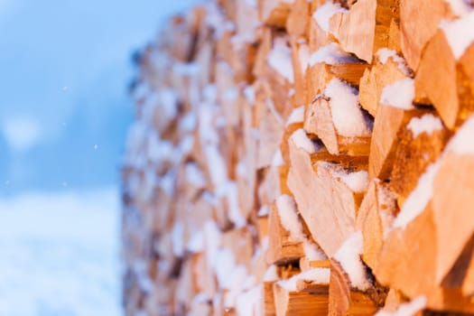 Full-sized side view of freshly beaten, stacked and snow-covered firewood in front of evening mountainous background.