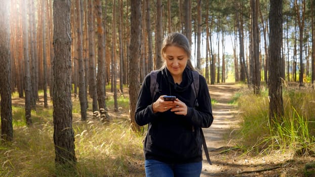 Portrait of beautiful smiling female tourist walking on hiking route and using navigator in smartphone.