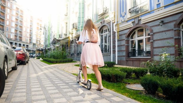 Beautiful young woman using kick scooter to travel in city.