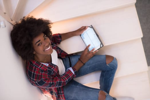 Attractive young black woman using her electronic tablet while sitting on a staircase