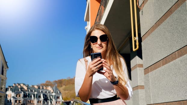 Portrait of beautiful young woman in sunglasses typing message on smartphone.