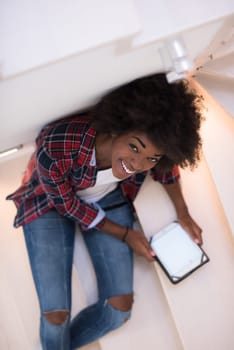 Attractive young black woman using her electronic tablet while sitting on a staircase