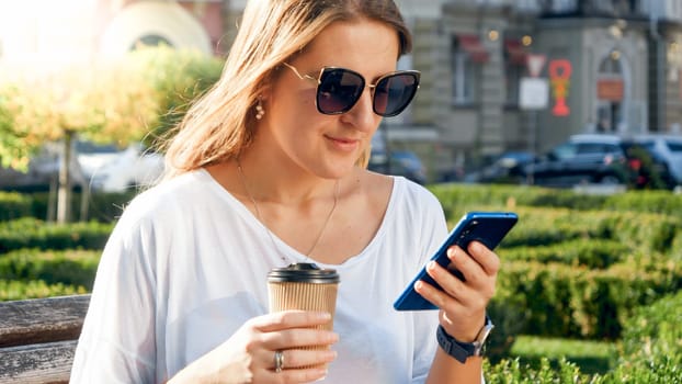 Portrait fo stylish young woman relaxing in park and drinking coffe from paper cup.