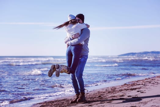 Young couple having fun walking and hugging on beach during autumn sunny day