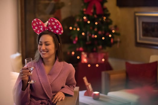 people, and relaxation concept   beautiful young woman in bath robe drinking champagne at spa over holidays lights background