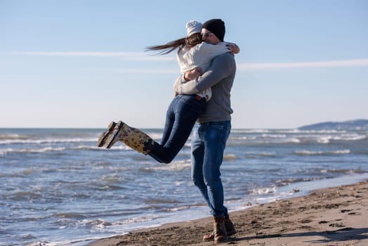 Young couple having fun walking and hugging on beach during autumn sunny day