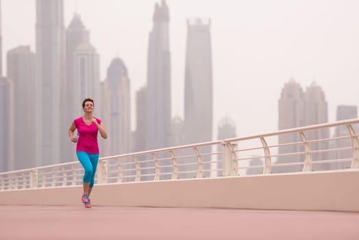 very active young beautiful woman busy running on the promenade along the ocean side with a big modern city in the background to keep up her fitness levels as much as possible