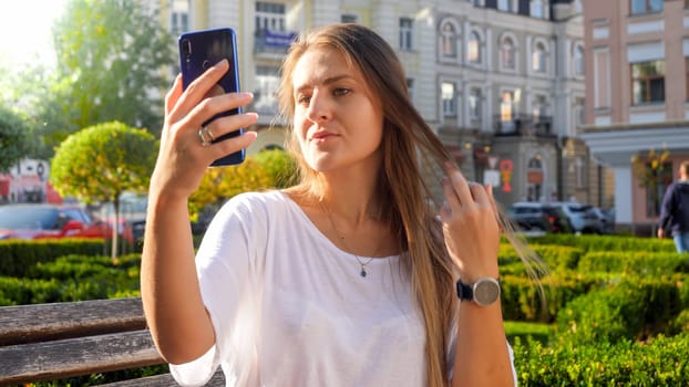 Portrait of beautiful young woman making selfie photo on smartphone in park.