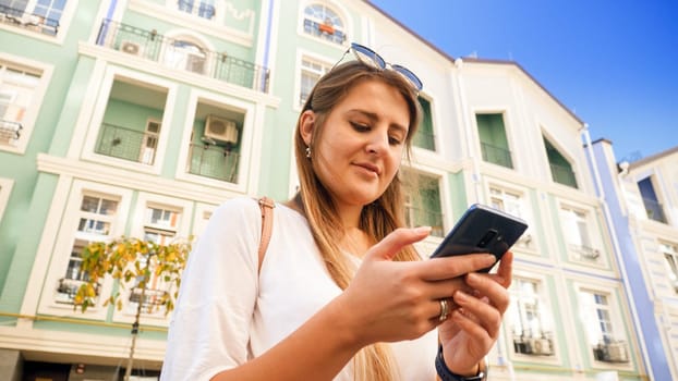 Portrait of beautiful smiling girl on city street using smartphone.