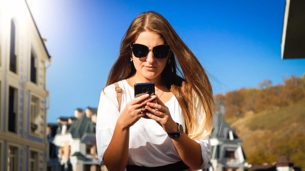Portrait of young concentrated woman typing message on smartphone on city street.