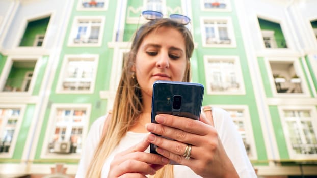 Closeup image of young woman holding smartphone in hands on city street.