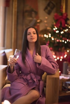 people, and relaxation concept   beautiful young woman in bath robe drinking champagne at spa over holidays lights background