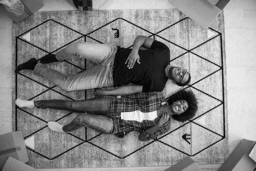 Top view of attractive young African American couple moving, holding hands, looking at camera and smiling while lying among cardboard boxes
