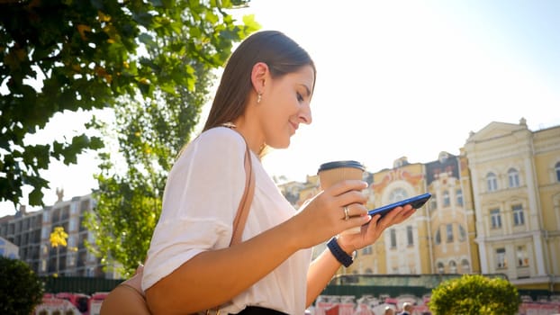 Portrait of beautiful female student walking in park with coffe and smartphone.
