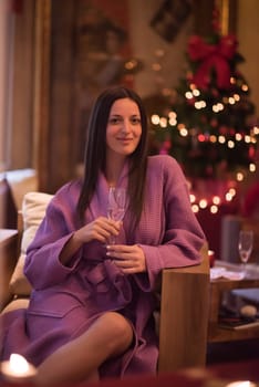 people, and relaxation concept   beautiful young woman in bath robe drinking champagne at spa over holidays lights background