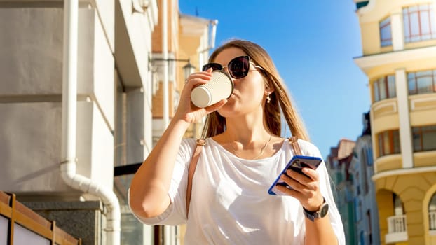Portrait of young busy woman walking on street and drinking coffee from disposable paper cup.