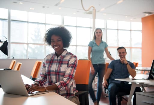 young smiling African American informal businesswoman working in the office with colleagues in the background