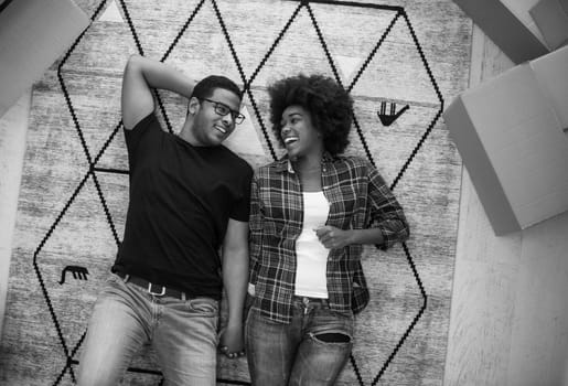 Top view of attractive young African American couple moving, holding hands, looking at camera and smiling while lying among cardboard boxes