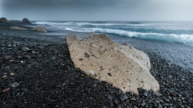 Rocks and cliffs on deserted volcanic ocean beach on cold windy day.
