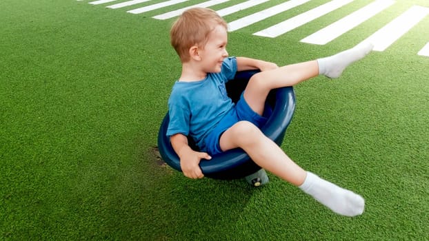 Happy smiling and laughing little boy sitting on rotating chair carousel on the playground.
