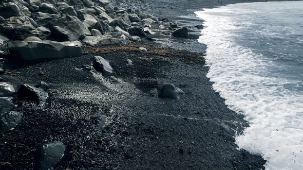 Landscape of black rocks and cliffs on volcanic sea beach.
