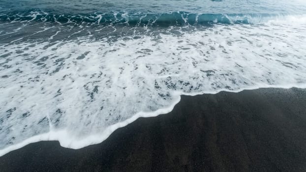 Beautiful image of blue ocean waves rolling and breaking on the beach with black volcanic sand.