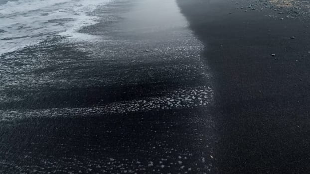 Closeup abstract image of wet black volcanic sand on the ocean beach.