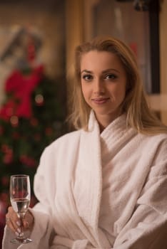 people, and relaxation concept   beautiful young woman in bath robe drinking champagne at spa over holidays lights background