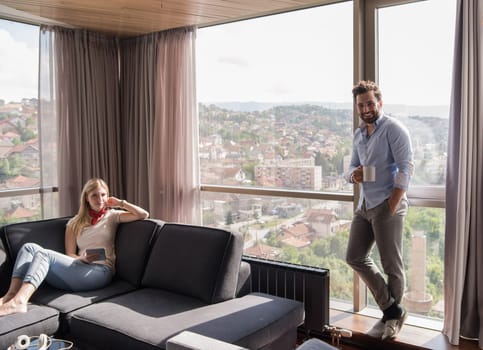 Young couple relaxing at  home using tablet computer reading in the living room near the window on the sofa couch.