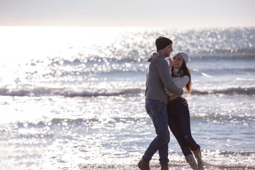 Young couple having fun walking and hugging on beach during autumn sunny day