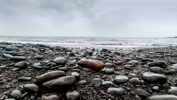 Beautiful landscape of wet pebbles and rocks lying on ocean shore at cloudy day.