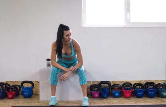 young athlete woman sitting and relaxing after exercise at cross fitness gym