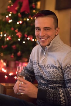 Portrait of a happy young man with a glass of champagne celebrating winter holidays at home beautifully decorated for Christmas
