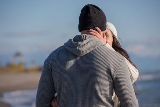 Young couple having fun walking and hugging on beach during autumn sunny day