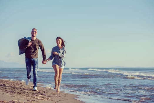 Young couple having fun walking and hugging on beach during autumn sunny day